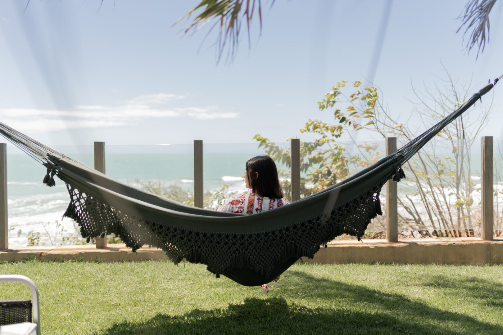 Hóspede relaxa em rede com vista para o mar no Carmel Charme Resort, simbolizando o turismo de bem-estar em contato com a natureza.