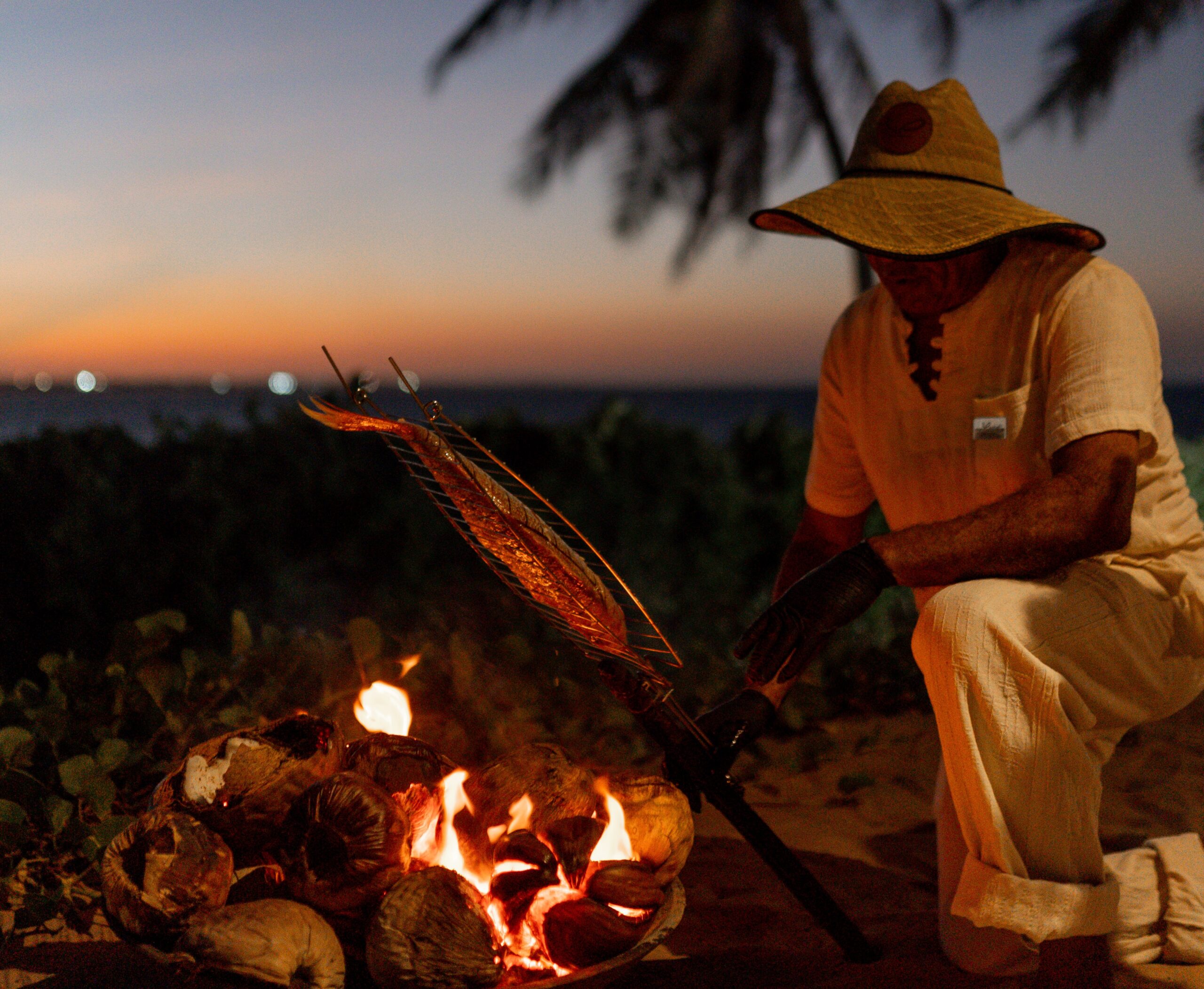 Pescador assando peixe na brasa do coco seco enquanto conta suas histórias