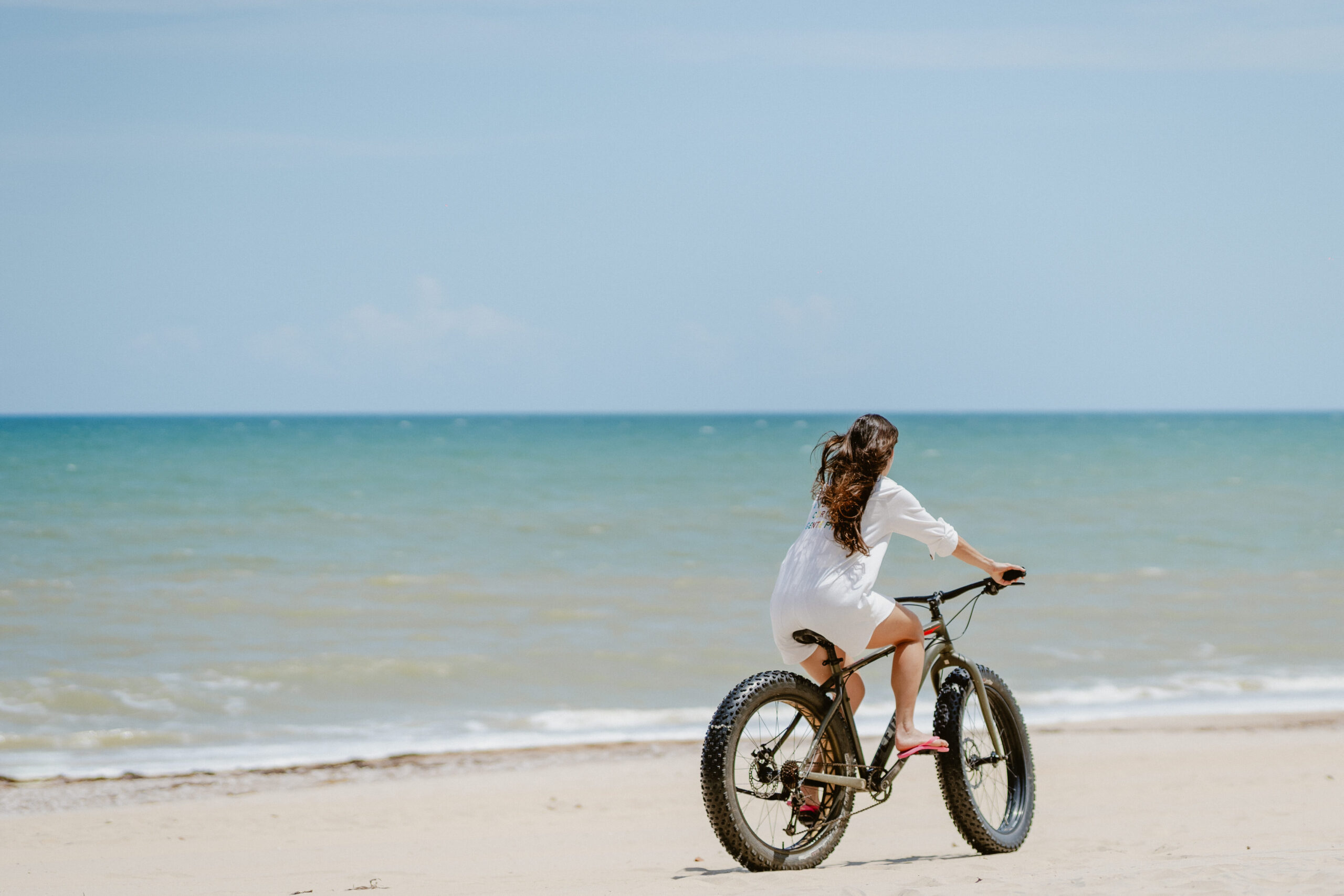 Mulher pedalando uma bicicleta adaptada para areia da praia sentindo o vento sob seus cabelos na praia 