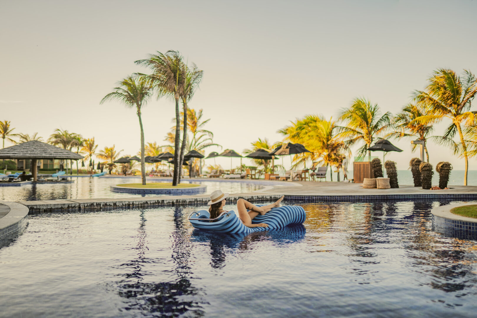 Mulher deitada em uma boia azul dentro da piscina ampla que fica de frente para o mar em sua viagem solo