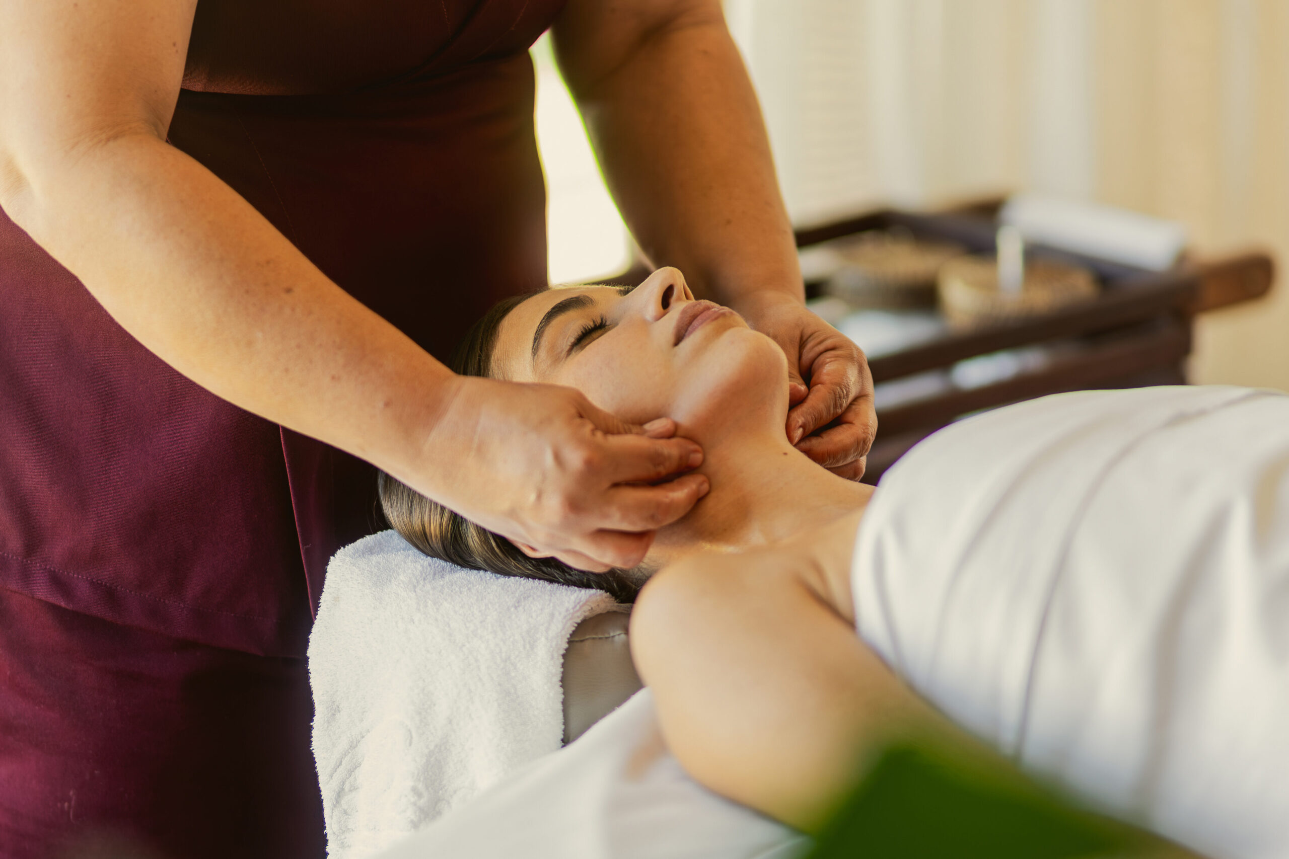 Mulher deitada em uma mesa de massagem enquanto as mãos da massagista massageiam seu rosto em sua viagem solo