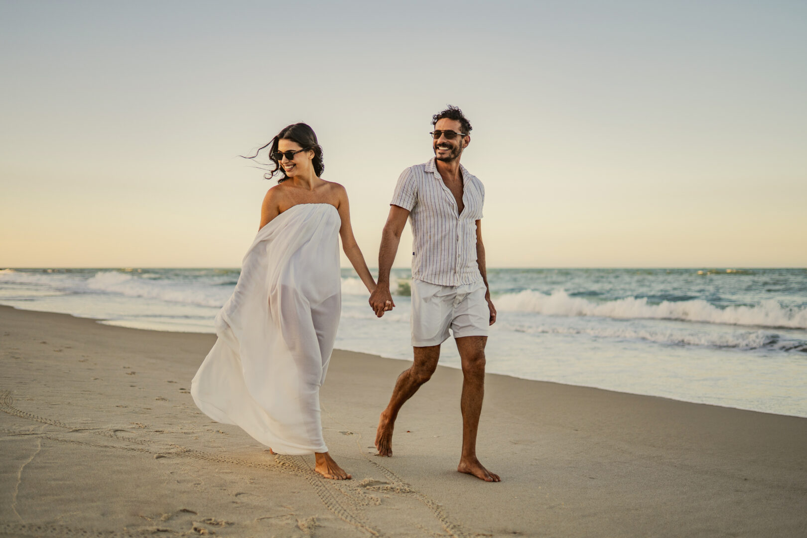 Casal com pés descalços caminhando pela areia à beira-mar em uma viagem em família