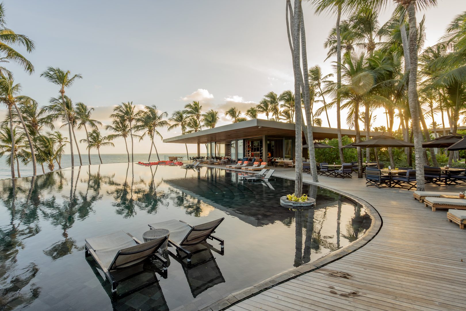 Ceará em janeiro: vista da piscina e do deck com espreguiçadeiras e guarda-sóis, cercados por coqueiros diante da praia.